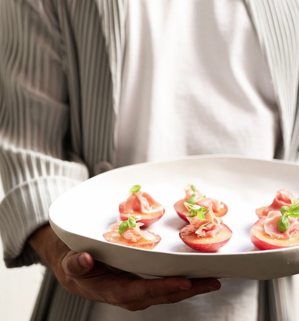 Waiter presenting a white plate of stone-fruit and prosciutto canapés
