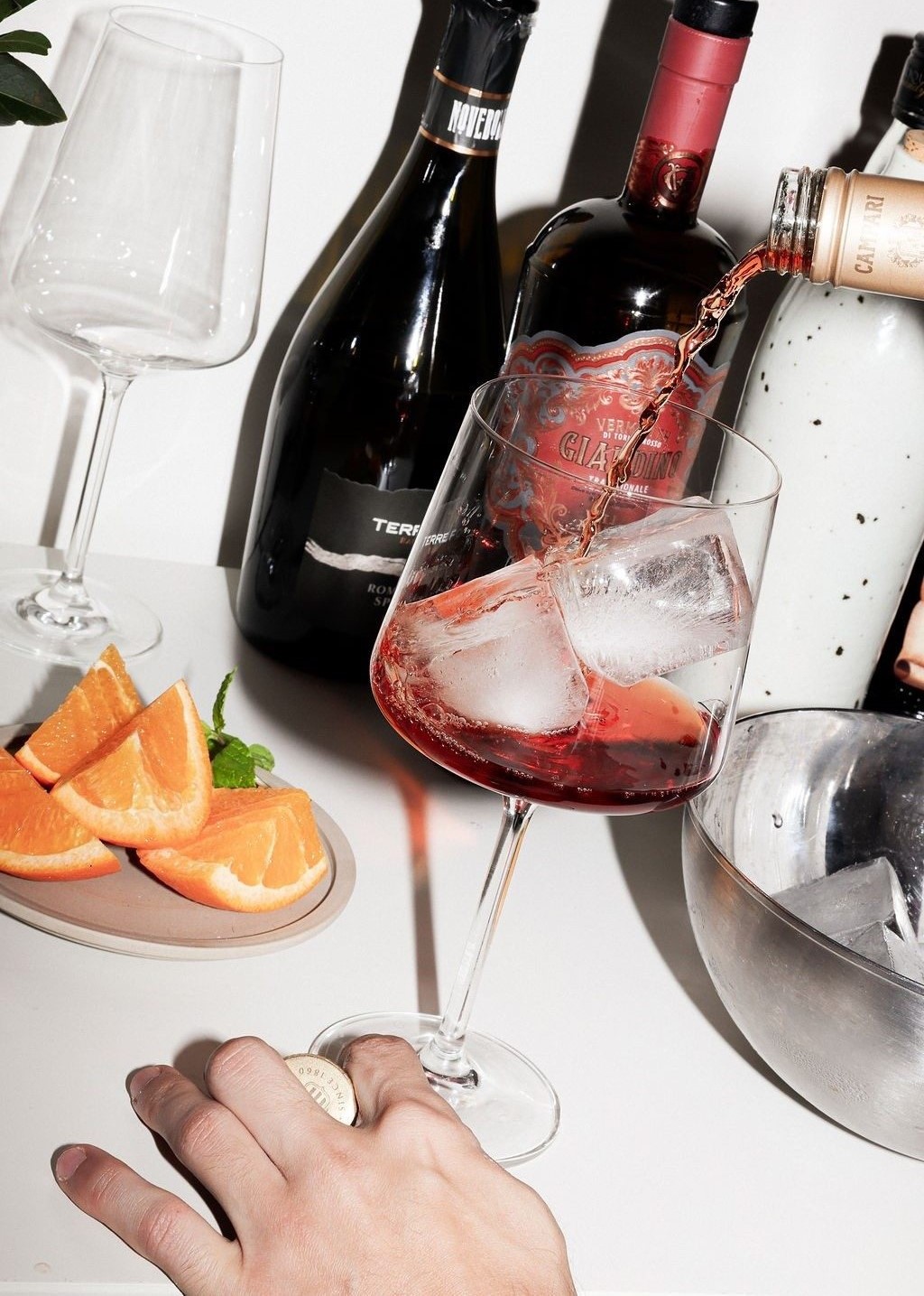 Negroni being poured over ice with orange and Campari bottles on a styled bar table